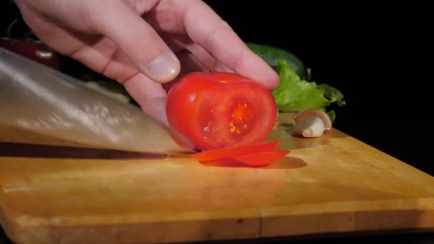 Mens mãos cortadas tomate com uma faca em pedaços na placa de corte em um fundo preto — Vídeo de Stock