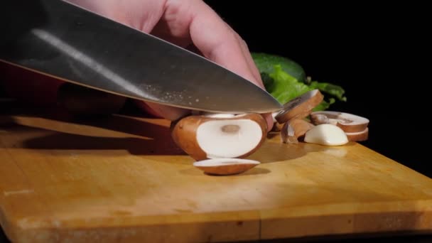 Mens mãos cortadas champignon com uma faca em pedaços na placa de corte em um fundo preto — Vídeo de Stock