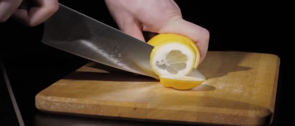 Mens hands cut fresh juicy lemon with a knife into pieces on cutting board on a black background — Stock Video