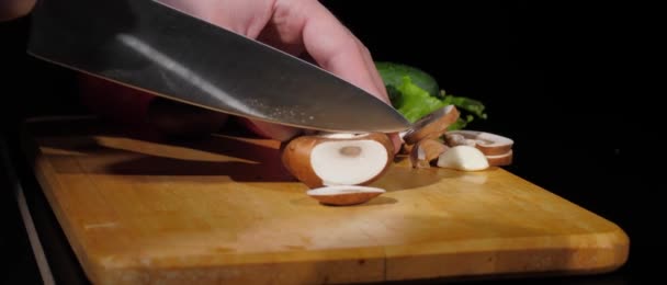 Pánské ruce pečlivě řezané champignon s nožem na kousky na řezací desce na černém pozadí — Stock video