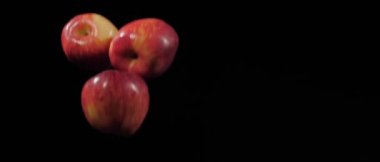 Üç taze kırmızı elmadan oluşan bir grup ağır çekimde siyah bir arka planda uçuyor.