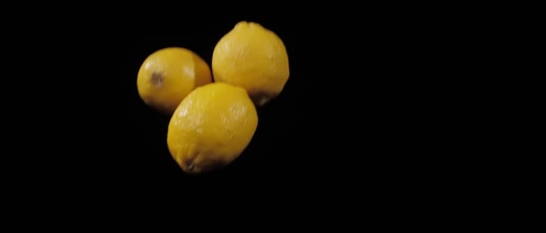 Tři čerstvé citrony hodil nahoru a létat na černém pozadí ve zpomaleném záběru — Stock video