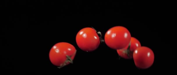 Cinco tomates frescos jogados para cima e voam com gotas de água em um fundo preto em câmera lenta — Vídeo de Stock