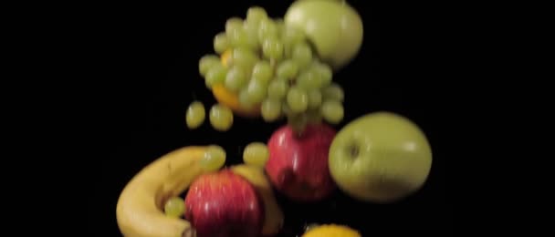 Uve fresche, mele, banane, limone e pere lanciati e volare in giro su uno sfondo nero in slow motion shot — Video Stock