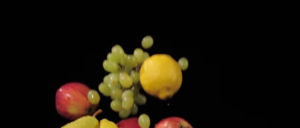 Uvas frescas y sabrosas, manzanas, plátanos, limón y peras batidas y volando sobre un fondo negro en cámara lenta, salpicaduras de agua en las frutas — Vídeos de Stock