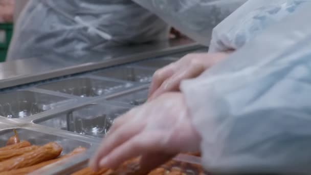 Zbliżenie na pracowników zakładu przetwórstwa mięsnego umieszczanie gotowych kiełbasek w plastikowych opakowaniach — Wideo stockowe