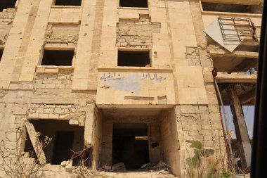 08.08.2025. Halep, Suriye. Savaştan zarar görmüş güvenlik binası, kısmen silinmiş Arapça graffiti yazılarıyla (Esad 'ın Adamları, sadık askerler). Çatışmanın, gücün ve tarihsel hafızanın güçlü görsel sembolü.