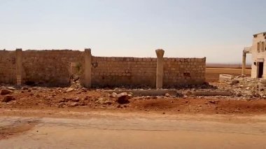 Suriye 'nin Halep kentindeki savaş hasarlı köyde, çöken taş duvarlar ve terk edilmiş tarım arazilerinin yanından geçerken görülüyor. Sahne çatışmanın uzun vadeli etkisini vurguluyor ve belgesel için ideal..