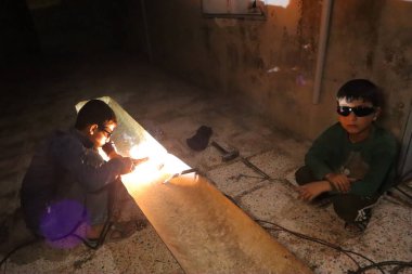 Halep, Suriye savaşın etkilerinden dolayı iki çocuk güvenli olmayan koşullarda metal kaynak yapıyor. Bu sahne yoksulluğu, hayatta kalmayı, tehlikeyi ve çocuk işçiliğini yansıtıyor..