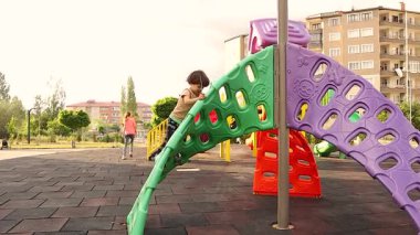 Parkta oyun parkında oynayan bir çocuk. Aniden çocuk heyecanla Arapça ilahi söylüyor, başını dik tut, özgür bir Suriyeli oluyorsun, yurtdışında büyürken neşe, gurur, özgürlük ve kimliğini ifade ediyorsun.