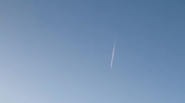 Sivil jet uçağı açık havada uzun bir iz bırakarak, hava yolculuğunu, havacılık fiziğini, iklim etkisini, teknolojiyi, küresel ulaşımı, hızı, irtifayı ve modern endüstri geçmişini sembolize ediyor..