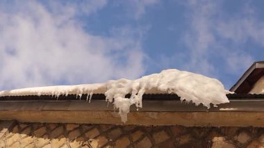 Kanada 'da ilkbaharın başında mavi bir gökyüzünün altında eriyen kar ve buz saçakları bir evin çatısından damlıyor. Mevsimsel erime, iklim değişikliği konsepti, kış geçişi, su damlaları, düşen buz tehlikesi. Hava, çevre ve mevsimlik temalar için ideal.