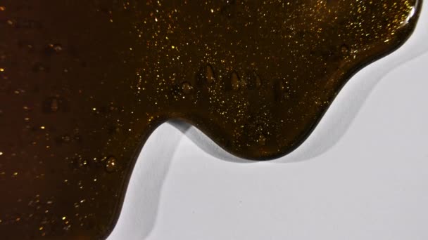 Cokelat kosmetik gel cair emas diselingi mengalir dengan turun pada permukaan putih. Macro Ditembak — Stok Video