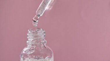 Pembe arka planda izole bir şekilde tıbbi bir şişedeki pipetten düşüyor.