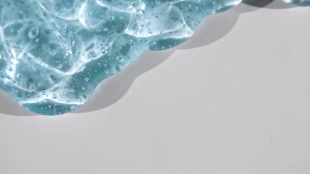 Líquido de gel azul transparente con burbujas que fluyen hacia abajo sobre una superficie blanca. Macro Shot — Vídeo de stock