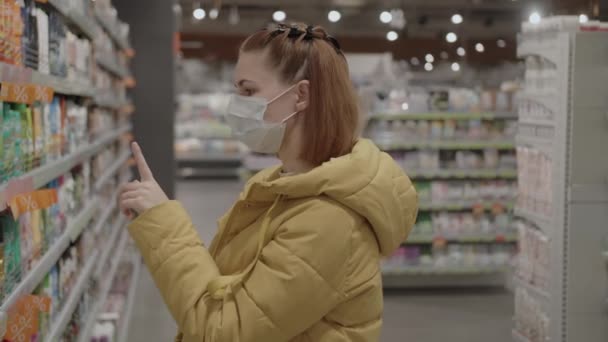 Kvinna i skyddande medicinsk mask väljer hygienartiklar i snabbköpet under covid-19 coronavirus epidemi. Shopping under karantänen, coronavirus COVID-19 pandemi. — Stockvideo