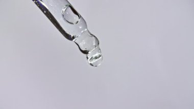 Gri zemin üzerinde yağ damlaları olan kozmetik pipeti
