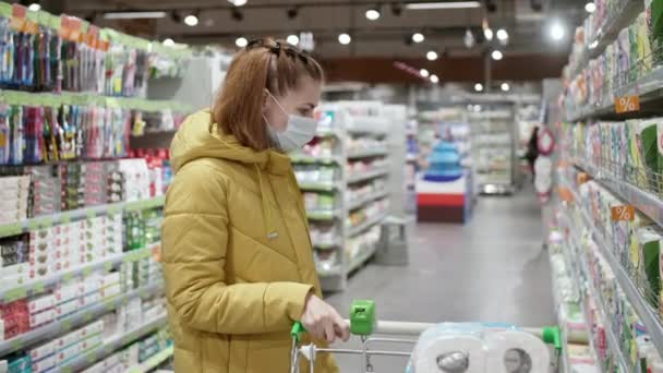 Frau in medizinischer Schutzmaske wählt während der Coronavirus-Epidemie im Supermarkt Hygieneartikel aus. Einkaufen während der Quarantäne, Coronavirus COVID-19 Pandemie. — Stockvideo