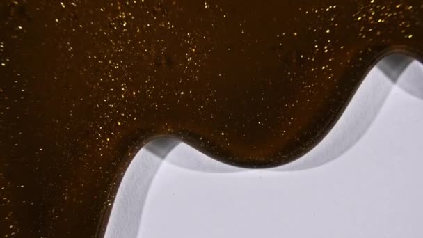 Hnědá kosmetická gelová tekutina, protékající zlatem po bílém povrchu. Makro snímek — Stock video