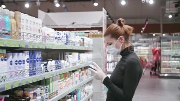 Een vrouw met een beschermend medisch masker kiest hygiëneartikelen in een supermarkt tijdens de covid-19 coronavirus epidemie. Veilig winkelen tijdens quarantaine, COVID-19 coronavirus pandemie. — Stockvideo