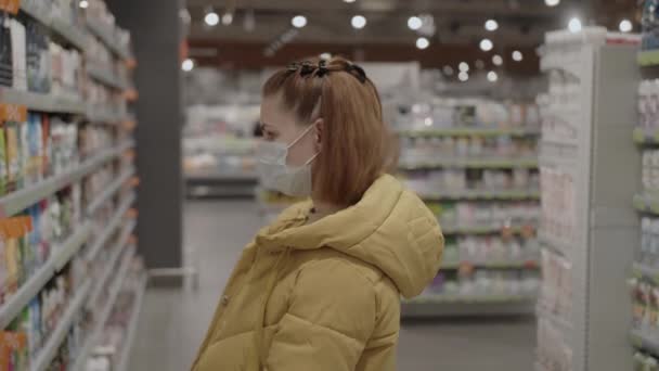Koruyucu tıbbi maskeli bir kadın, covid-19 koronavirüs salgını sırasında süpermarketten hijyen ürünleri seçiyor. Karantina sırasında alışveriş, Coronavirus COVID-19 salgını. — Stok video