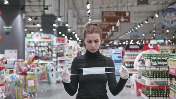 Een jonge aantrekkelijke vrouw met een beschermend masker in de winkel. Proces van vrouwelijk aanbrengen van gezichtsmasker. — Stockvideo