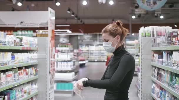 Mladá žena v ochranné lékařské masce si nasazuje rukavice ve zpomaleném filmu. Bezpečné nakupování během karantény, pandemie koronaviru. — Stock video