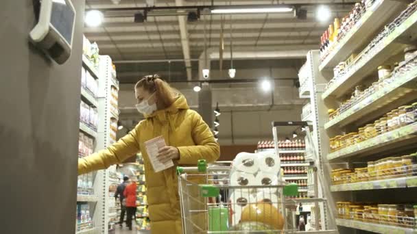 Koruyucu tıbbi maskeli bir kadın, covid-19 koronavirüs salgını sırasında süpermarketten hijyen ürünleri seçiyor. Karantina sırasında alışveriş, Coronavirus COVID-19 salgını. — Stok video