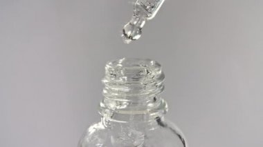 Tıbbî bir şişedeki pipetten düşüş yakın plan, gri arka planda izole edilmiş.