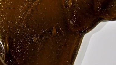 Kahverengi kozmetik sıvı altın karışımı beyaz bir yüzeye akıyor. Makro Vuruş