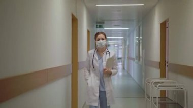 Maskeli bir doktor hastane koridorunda yürüyor.