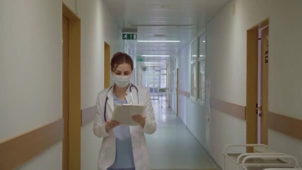 Maskovaný doktor kráčí chodbou nemocnice. — Stock video