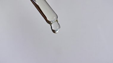 Gri zemin üzerinde yağ damlaları olan kozmetik pipeti