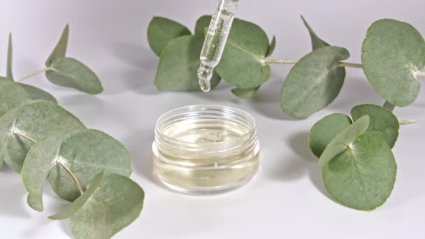 Pipette mit Eukalyptusöl mit Blättern auf weißem Hintergrund. Eukalyptusextrakt, aromatisches ätherisches Öl. Naturkosmetik für Haar- und Hautpflege. Ansicht von oben. — Stockvideo