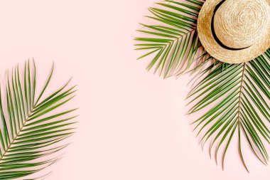 Yaz dönemi. Tropik palmiye yaprağı dalları, pembe arka planda hasır şapka ve mesaj için boş alan. Seyahat tatili konsepti. Düz yatış, üst görünüm.