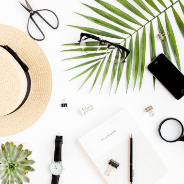 Üst kat ofis masası. Hasır şapka, gözlük, retro kamera, not defteri ve beyaz arka planda tropikal palmiye yaprağı olan çalışma alanı. Düz yatış, üst görünüm.