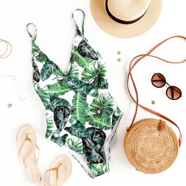 Kadın plaj aksesuarları: Tropikal desenli mayo, rattan çanta, beyaz arka planda hasır şapka. Yaz arkaplanı. 