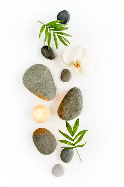 Spa stones, palm leaves, flower white orchid, candle and zen like grey stones on white background. Flat lay, top view