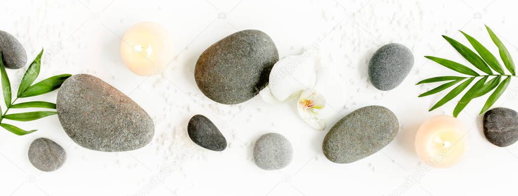 Spa stones, palm leaves, flower white orchid, candle and zen like grey stones on white background. Flat lay, top view