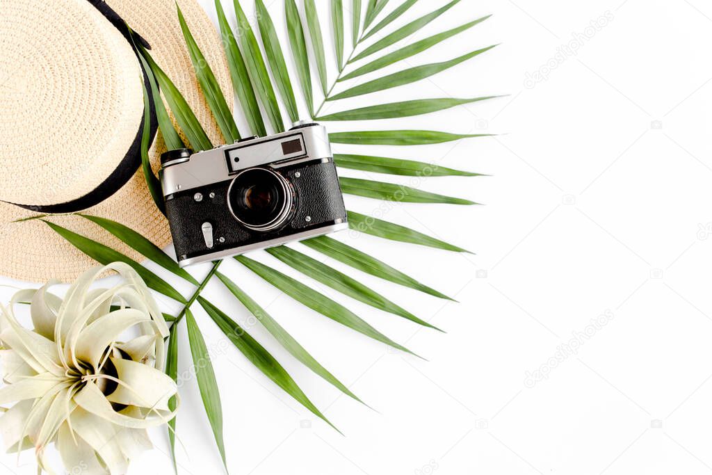 Flat lay traveler accessories on white background with retro camera, straw hat, sunglasses, and tropical palm leaf. Travel concept background. 