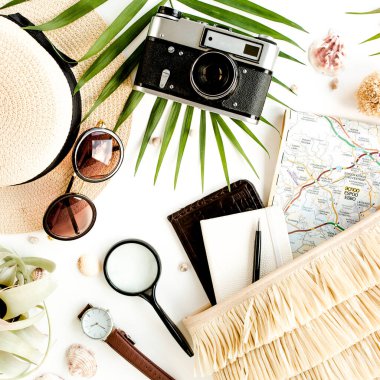 Retro kamera, hasır şapka, çanta, güneş gözlüğü, harita ve tropikal palmiye yaprağıyla beyaz arka planda gezgin aksesuarları.