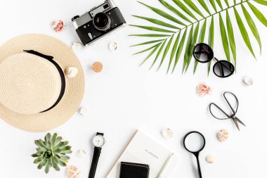 Üst kat ofis masası. Hasır şapka, gözlük, retro kamera, not defteri ve beyaz arka planda tropikal palmiye yaprağı olan çalışma alanı. Düz yatış, üst görünüm.