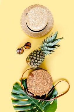 Kadın aksesuar gezgini: bambu çanta, hasır şapka, tropik palmiye yaprakları canavarı, sarı arka planda retro kamera. Düz yatış, üst görünüm