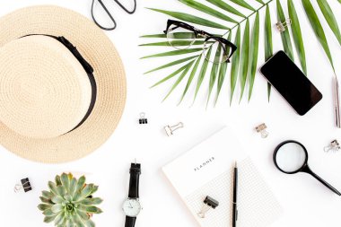 Üst kat ofis masası. Hasır şapka, gözlük, retro kamera, not defteri ve beyaz arka planda tropikal palmiye yaprağı olan çalışma alanı. Düz yatış, üst görünüm.