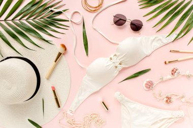 Kadınsı beyaz mayo plaj aksesuarları, pembe arka planda tropikal palmiye yaprağı dalları. Seyahat tatili konsepti. Yaz dönemi. Yol çerçevesi ayarlandı