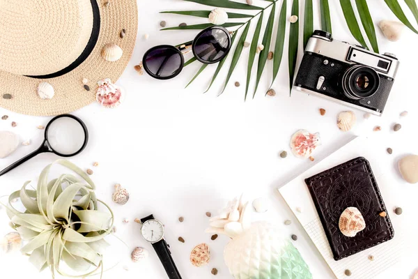 Аксессуары для путешественников на белом фоне с ретро-камерой, соломенной шляпой, солнцезащитными очками и тропическим пальмовым листом. Обязательные предметы для отдыха, концепция путешествия — стоковое фото