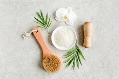 Spa konsepti. Doğal organik spa ürünleri, deniz tuzu, masaj fırçası ve yukarıdaki gri mermer masada tropik palmiye yaprakları. Spa arkaplanı