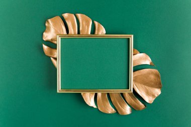 Altın tropikal palmiye yeşil arka planda Monstera ve fotoğraf çerçevesi bırakır. Düz konum, üst görünüm minimum konsept.