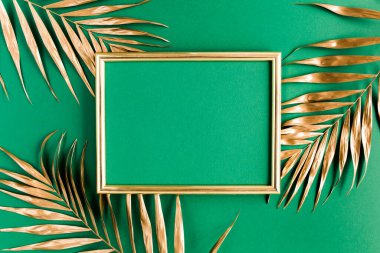 Altın tropikal palmiye yaprakları ve yeşil arka planda fotoğraf çerçevesi. Düz konum, üst görünüm minimum konsept.