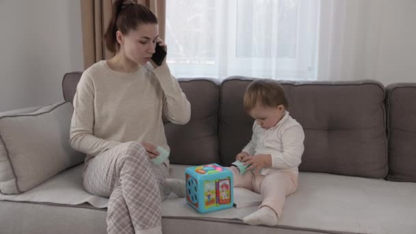 Madre trabajando desde casa, haciendo una videollamada de trabajo, hija jugando cerca. Quedarse en casa, poner en cuarentena el trabajo remoto. — Vídeos de Stock